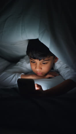 Vertical-Video-Close-Up-Of-Young-Boy-In-Bedroom-At-Home-Using-Mobile-Phone-To-Text-Message-Under-Covers-Or-Duvet-At-Night-1